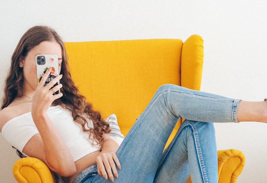 woman in white tank top and blue denim jeans sitting on yellow sofa