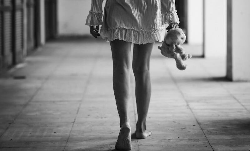 Black and white photo of a woman holding a doll, walking in a corridor.