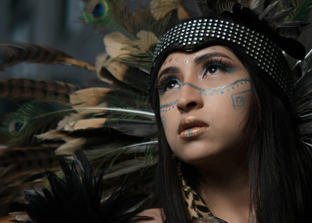 Close-up portrait of a woman wearing a traditional feather headdress, looking upward.