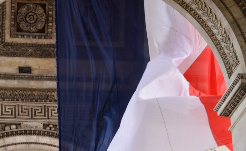a french flag flying in front of a stone arch