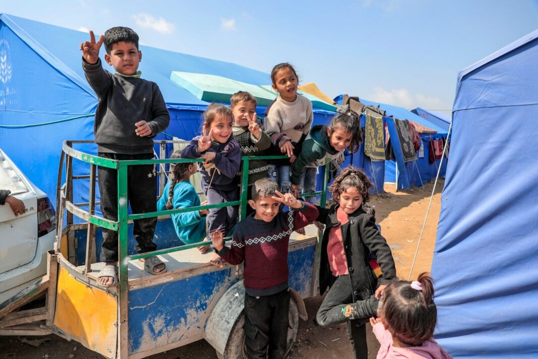 Smiling children pose in front of tents at a refugee camp