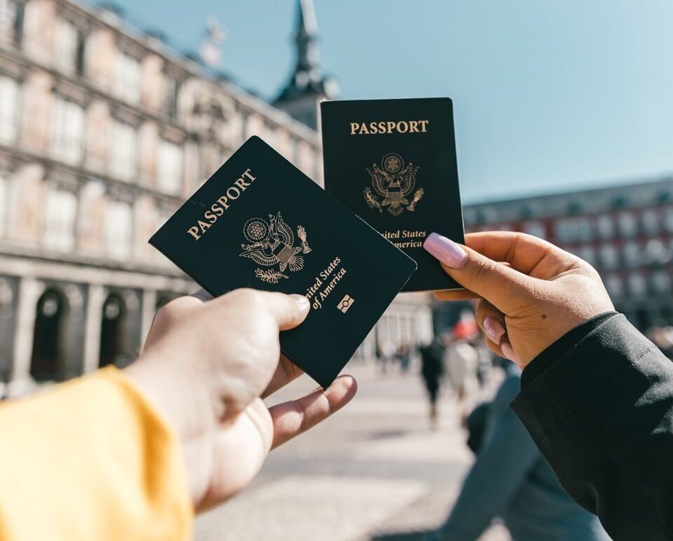 Crop unrecognizable travelers in casual clothes demonstrating passports of United States of America standing on square in historical city district