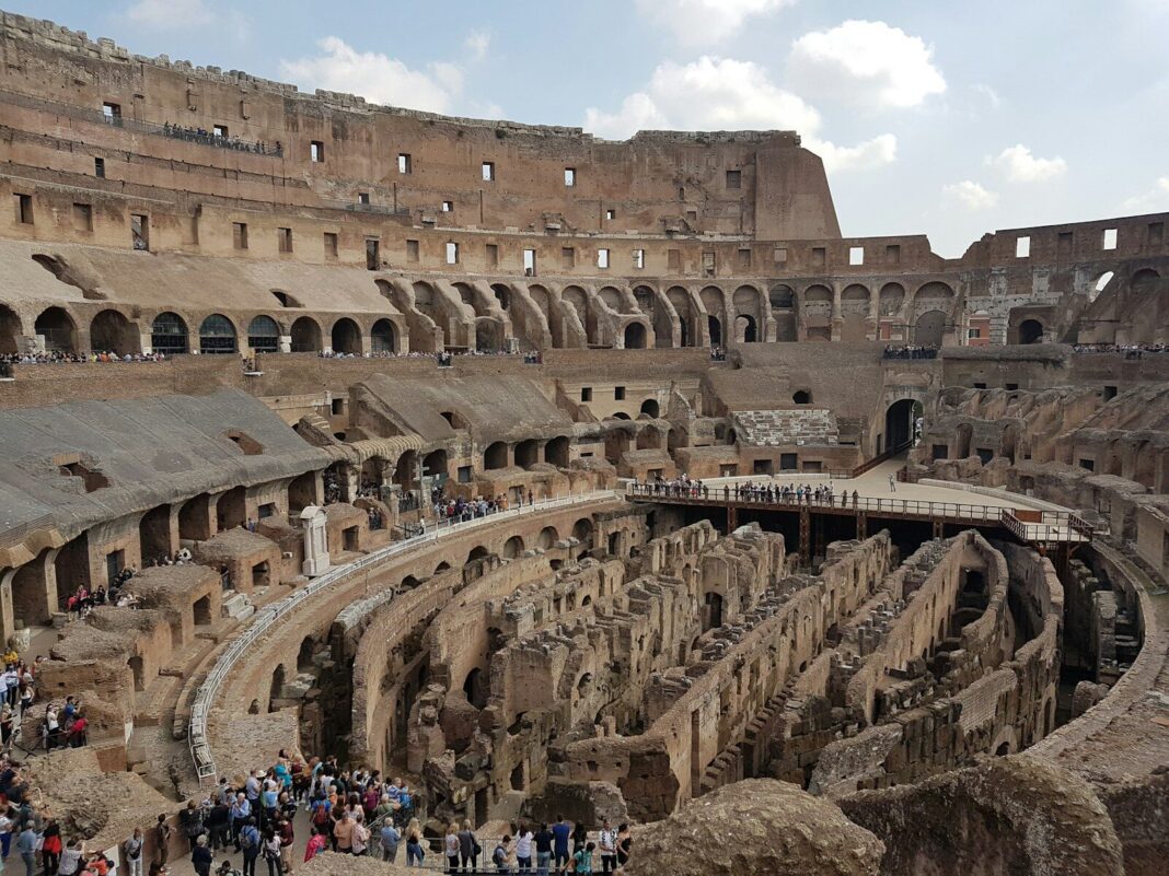 a large ancient building with many people in front of it with Colosseum in the background