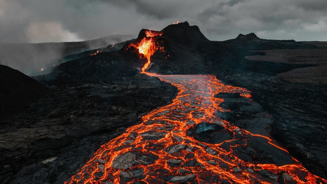 Molten lava flowing from the Fagradalsfjall volcano across a dark rocky landscape in Iceland