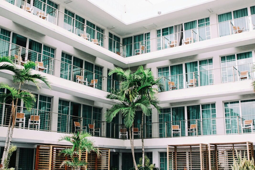A white multi-story hotel building with balconies and palm trees in a courtyard